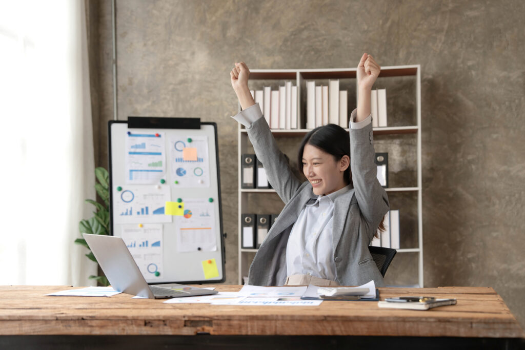 A young professional celebrating while sitting behind her desk and looking at her laptop